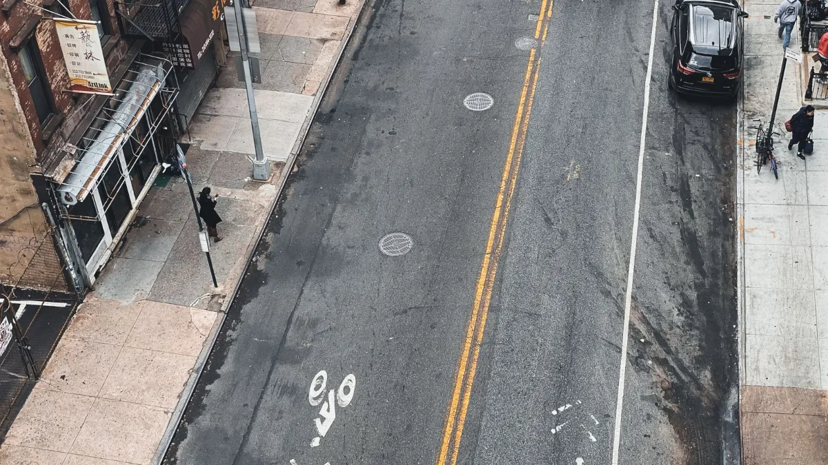 High-angle view of a city street showing painted bike lane markings, a crosswalk, and cars parked along the curb.