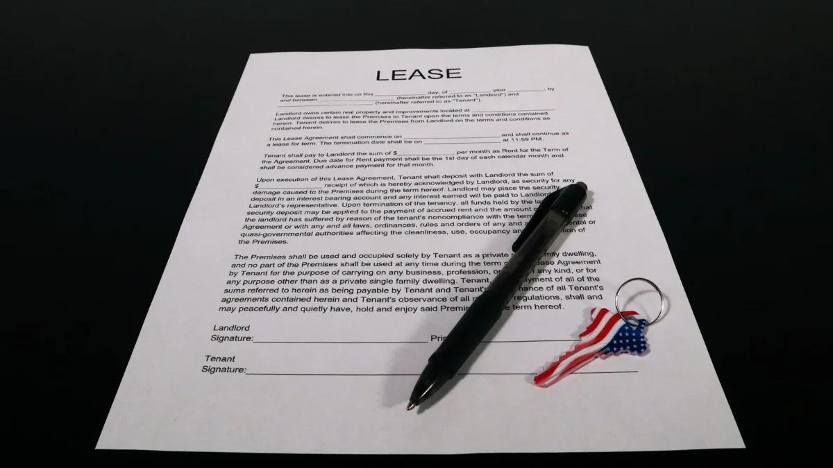 A lease agreement document with a pen and a keychain resting on a dark table
