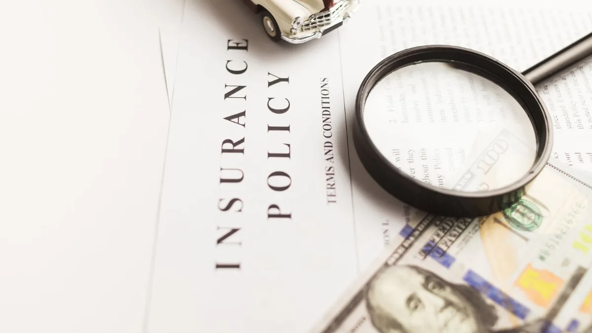A magnifying glass over an insurance policy document beside cash and a model car