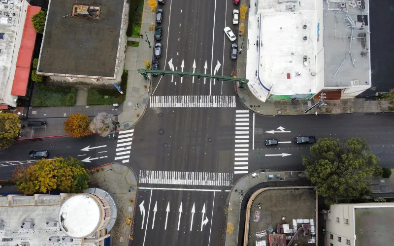 Overhead view of an urban intersection with cars crossing and lane markings interrupted through the junction