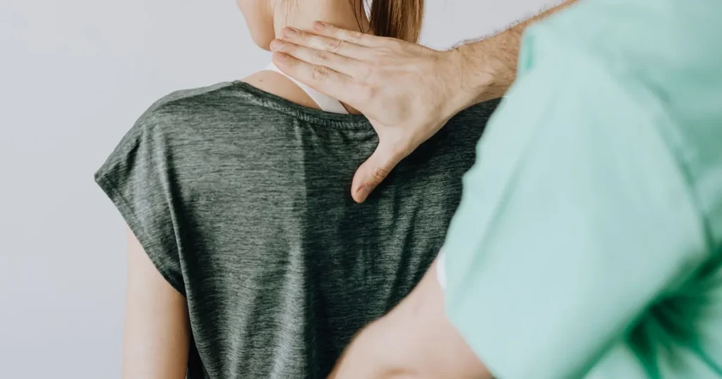 A clinician examining a patient's back and neck during a medical evaluation