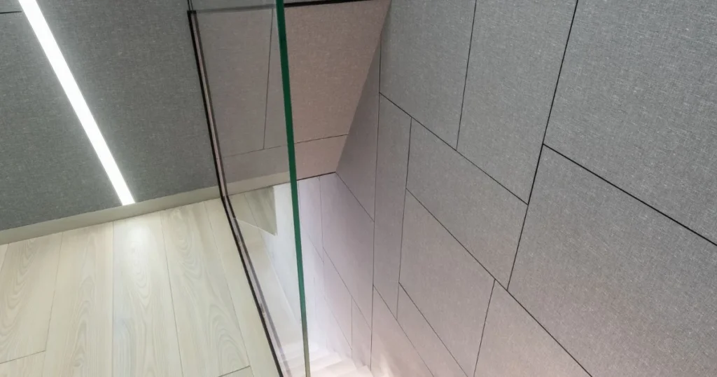 A modern interior staircase with a glass railing descending beside a gray wall.