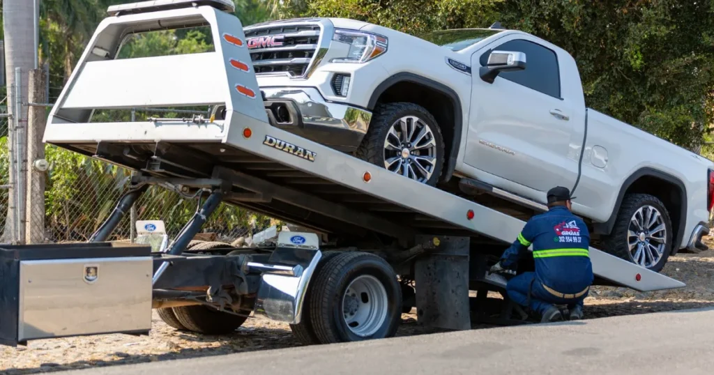 Tow truck operator loading a pickup truck onto a flatbed on a city street
