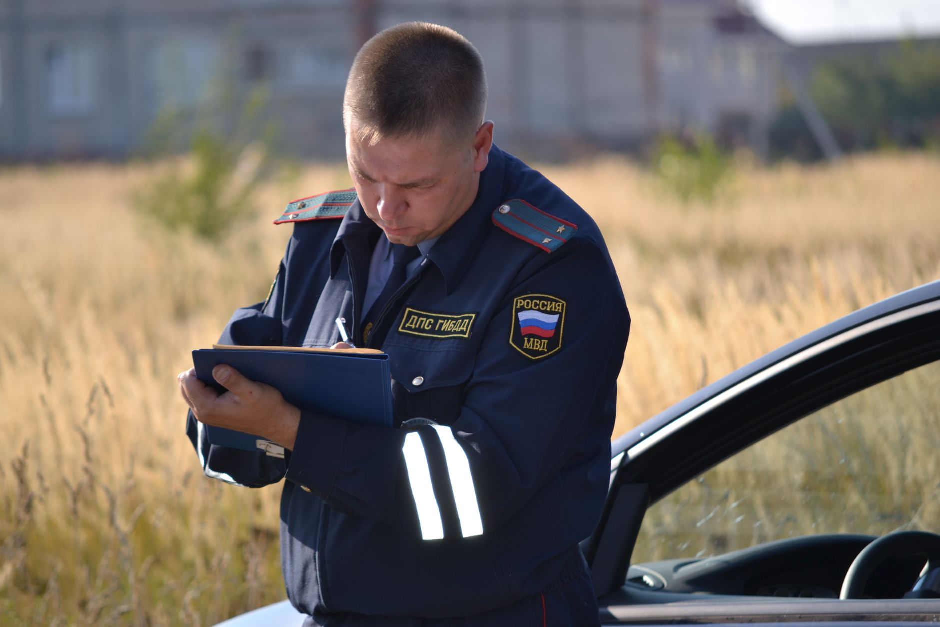 A uniformed officer standing beside a road writing notes on a clipboard after a collision