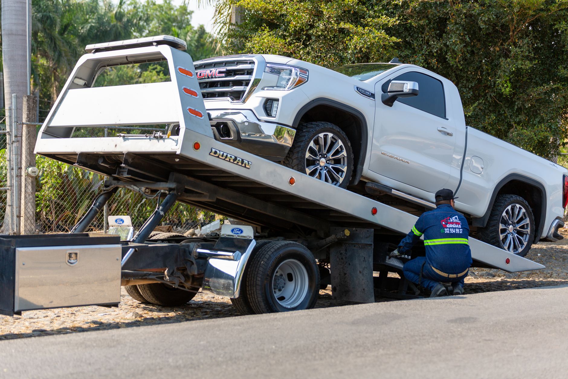 A tow truck with flashing amber warning lights winching a disabled car on a freeway shoulder