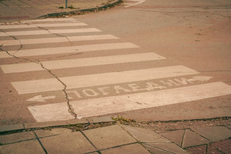 A cracked and uneven concrete sidewalk running alongside a city street