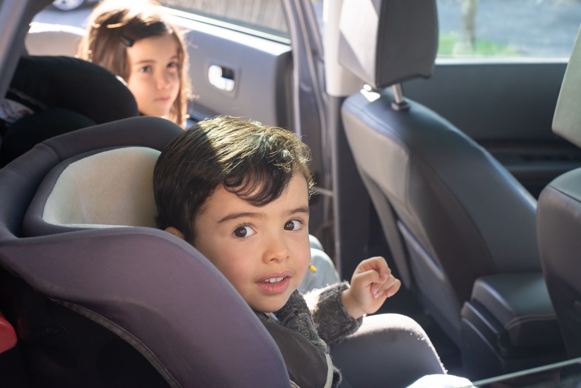 A young child buckled into a car seat in the rear seat of a vehicle