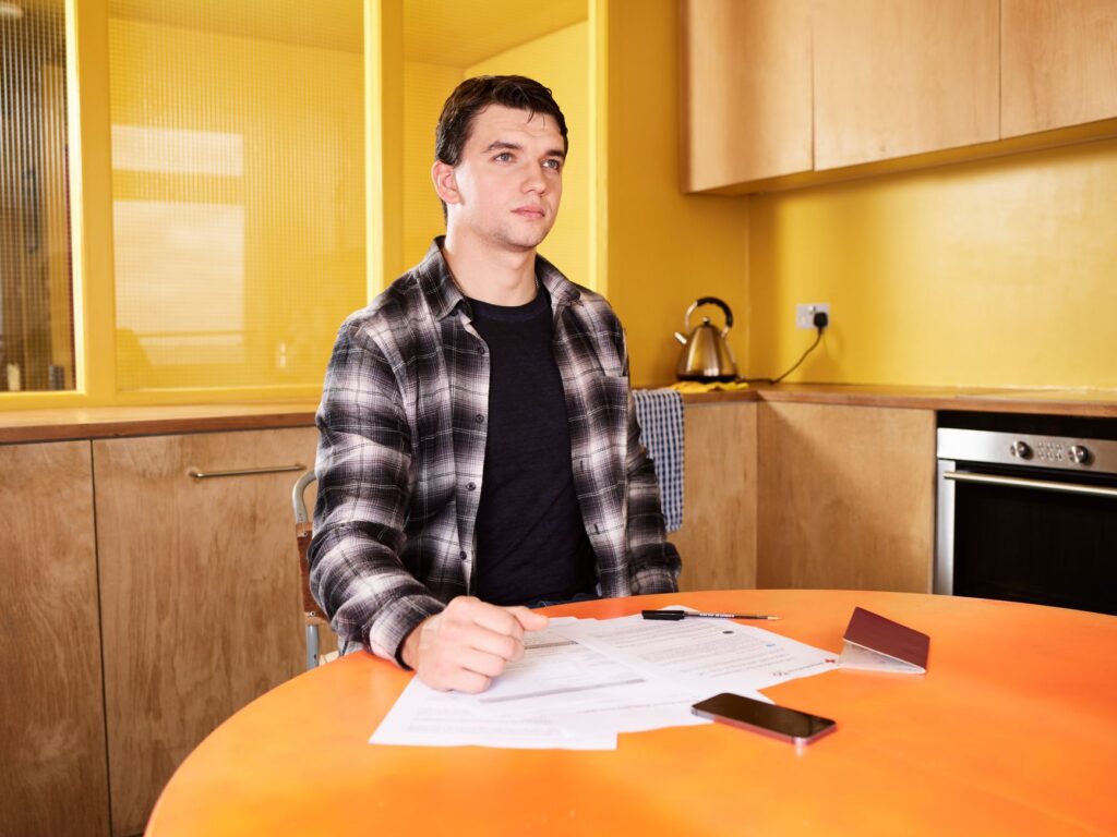 A person reviewing insurance paperwork at a kitchen table after a collision